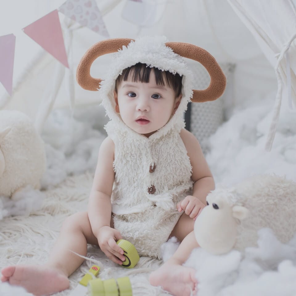 A toddler wearing a hat and sitting on a blanket